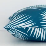A side shot of a palm printed outdoor cushion cover. The angle shows the edge of the square shape and the teal tone.