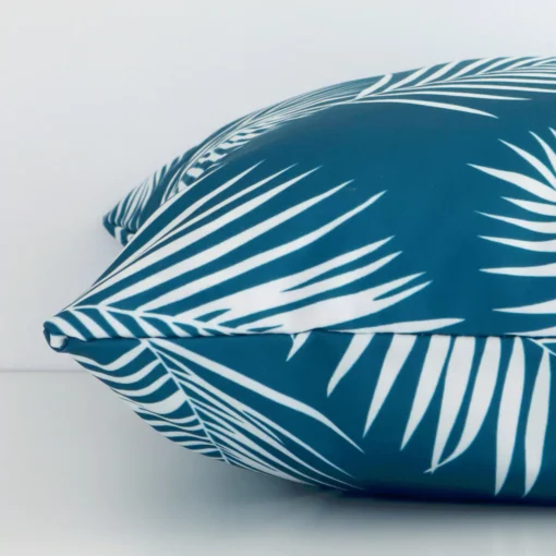 A side shot of a palm printed outdoor cushion cover. The angle shows the edge of the square shape and the teal tone.