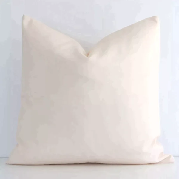 Solid-coloured square beige cushion positioned in front of a white wall. It is made of outdoor fabric.