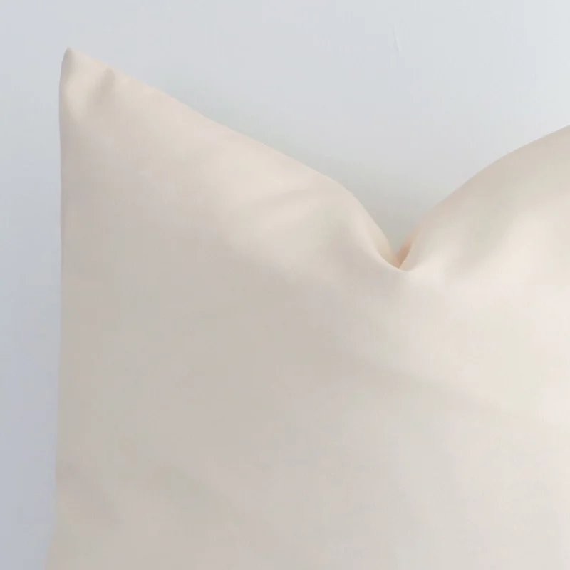 Close range image of beige solid-coloured cushion. The square size and outdoor material can be seen in detail.
