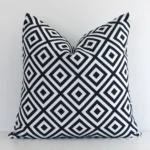An attractive geometric outdoor cushion in front of a white wall. It has a square shape and is black-and-white in colour.