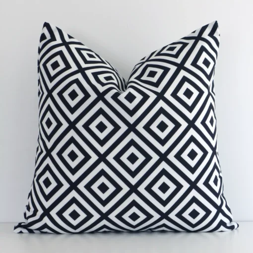 An attractive geometric outdoor cushion in front of a white wall. It has a square shape and is black-and-white in colour.