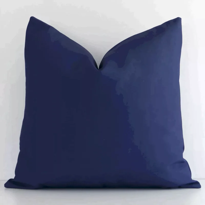 otama-waterproof-navy-outdoor-cushion-cover---sc710-45 White wall with a solid colour navy cushion laying against it. It has a distinctive outdoor fabric and has a square shape.