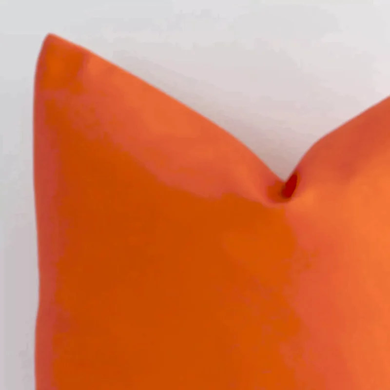Close up view showing a corner of this solid colour outdoor cushion in a square size and with orange colouring.