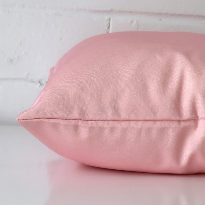 The seams of this outdoor square cushion cover in pink are shown.