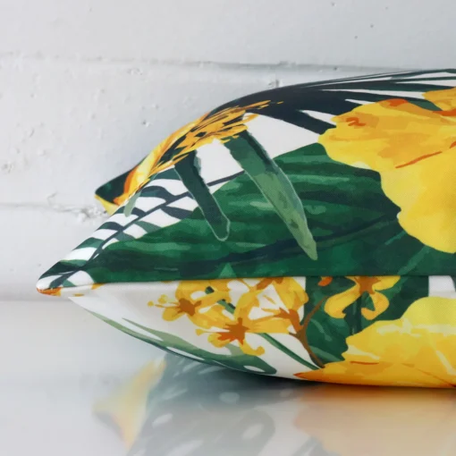 A yellow floral cushion arranged sideways in front of a wall. The square size and outdoor fabric are shown and the seams are clearly visible.