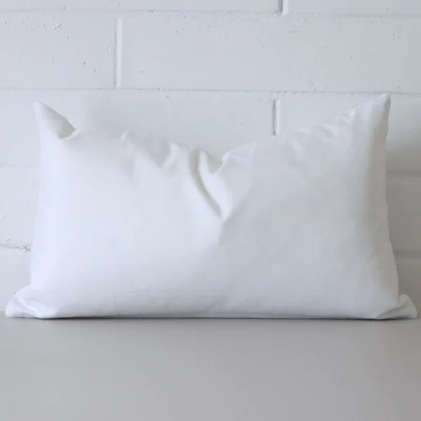 White cushion cover in front of a white wall. It has a rectangle size and is made from an outdoor material.