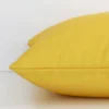 A yellow solid-coloured cushion arranged sideways in front of a wall. The square size and outdoor fabric are shown and the seams are clearly visible.