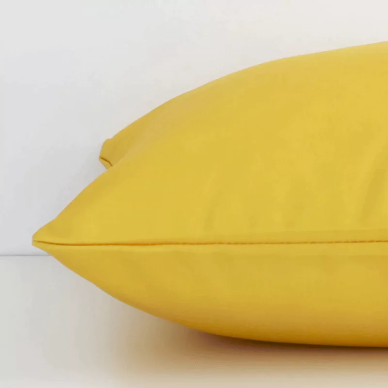 A yellow solid-coloured cushion arranged sideways in front of a wall. The square size and outdoor fabric are shown and the seams are clearly visible.