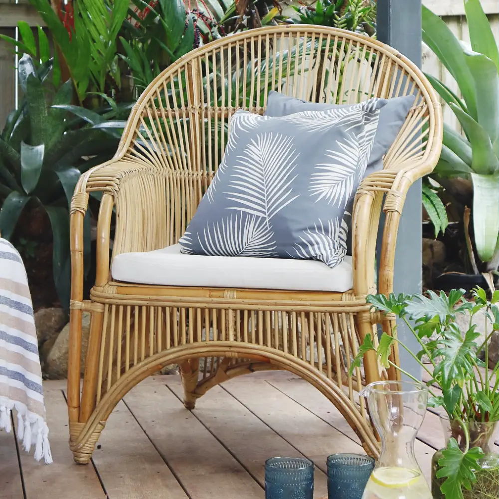 An outdoor rattan seat with two grey outdoor cushions on it.