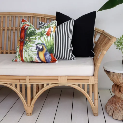 A rattan seat adorned with a set of 3 black outdoor couch cushions including cushions with a parrot and a stripe design.