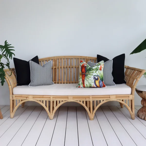 Five black outdoor cushions arranged on a rattan seat in a breezy lounge.