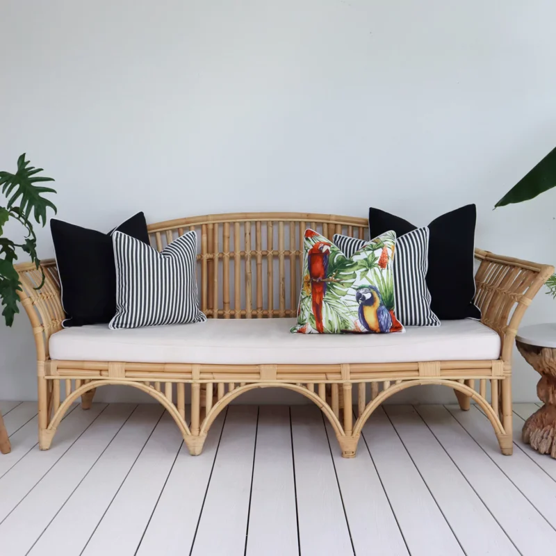 Five black outdoor cushions arranged on a rattan seat in a breezy lounge.