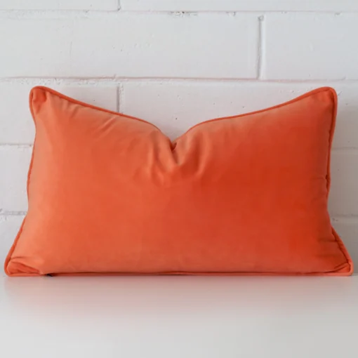 A lovely rectangle orange cushion cover arranged in front of a white wall. It is made from a velvet material.