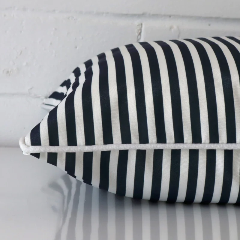 A square navy blue cushion cover laying flat. This viewpoint highlights the striped style and outdoor fabric from a side position.