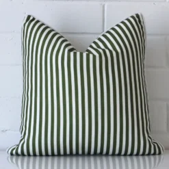 Here an olive green cushion is shown styled against a white wall. It has a square design and features a striped style.