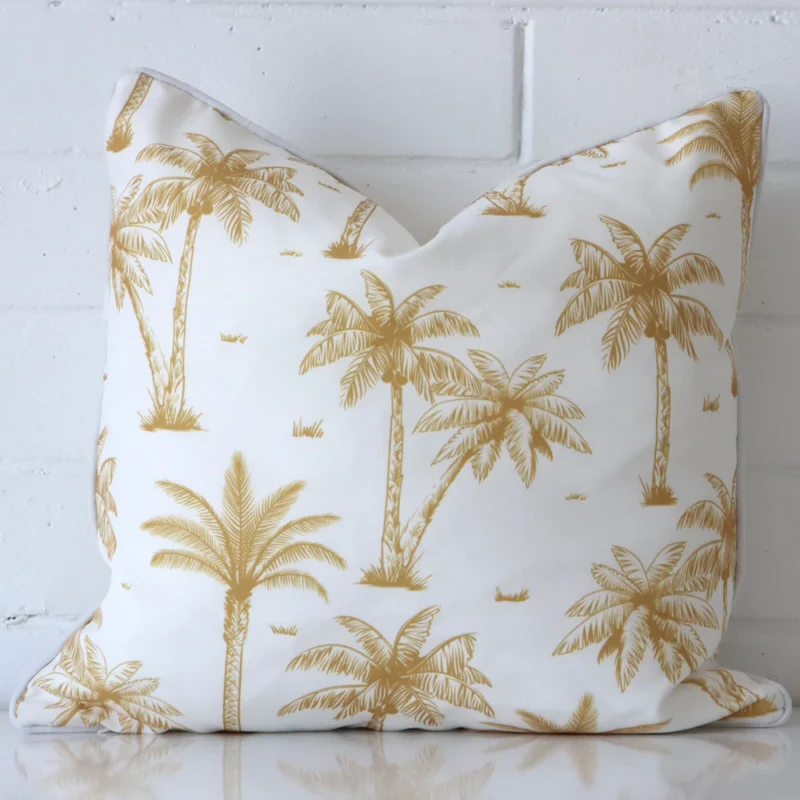 Mustard cushion leans elegantly against a brick wall. It has been crafted from a high quality outdoor material and has a square shape.