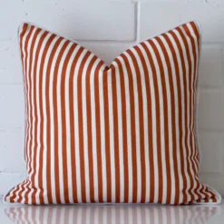 Terracotta cushion positioned in front of a brick wall. It has square dimensions and is made from an outdoor material.