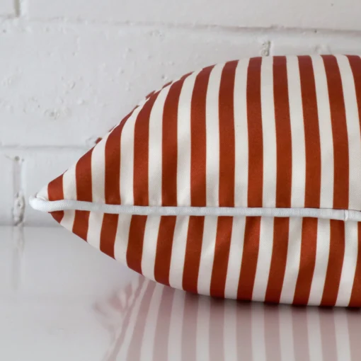 Side shot showing the seam of this square terracotta cushion that features a striped design on its outdoor material.