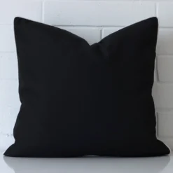 An outdoor large cushion cover that is shown vertically against a brick wall. It has a wonderful black colour.