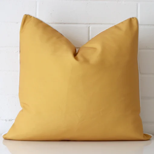 A large cushion in a delightful mustard tone rests against a white wall. The outdoor material appears to be of exceptional quality.