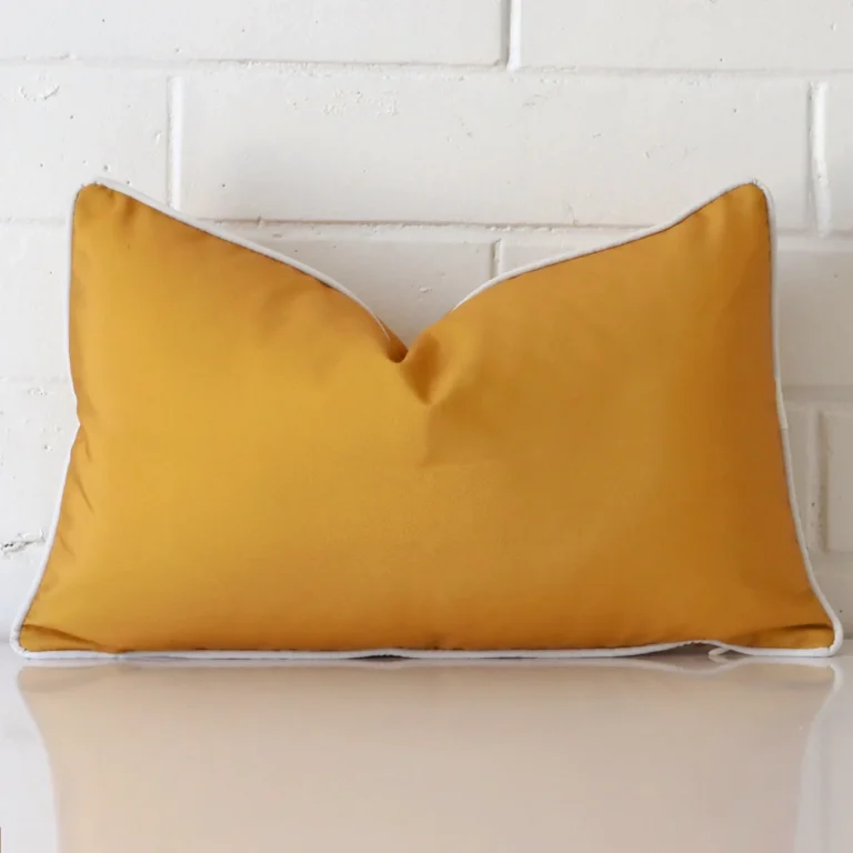 Mustard cushion leans elegantly against a brick wall. It has been crafted from a high quality outdoor material and has a rectangle shape.