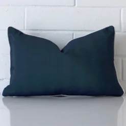 A pretty outdoor cushion cover is shown against a brick wall. It features a rectangle shape and a navy blue colour finish.