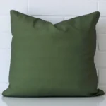 Olive green cushion leans elegantly against a brick wall. It has been crafted from a high quality outdoor material and has a large size.