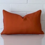 A lovely rectangle terracotta cushion cover arranged in front of a white wall. It is made from a good quality outdoor material.