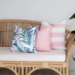 Three pink outdoor cushions are arranged at the end of a rattan seat.