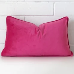 A velvet rectangle cushion cover that has a unique design is shown vertically against a brick wall. It has a wonderful pink colour.