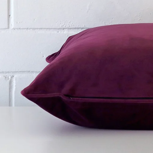 Horizontal edge view of front and back panels of a velvet cushion in a large size and with plum colouring.