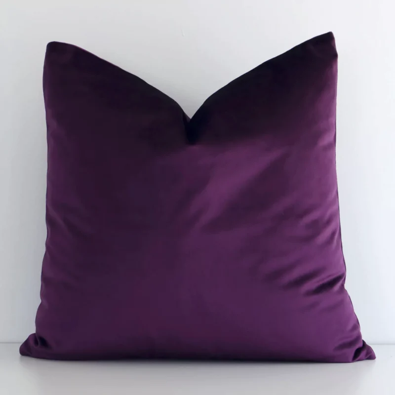 plum-purple-velvet-linen-cushion-cover---sc788-45 White wall with a solid-coloured plum cushion laying against it. It has a distinctive velvet fabric and has a square shape.