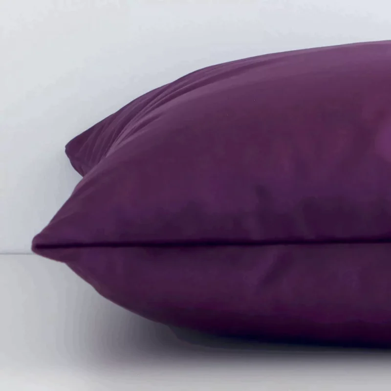 Velvet plum cushion laying on its side. The solid colour design and its square size are visible.