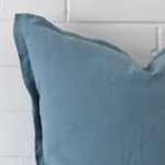 A zoomed in photo of the corner of a blue cushion that has linen fabric and a large size.
