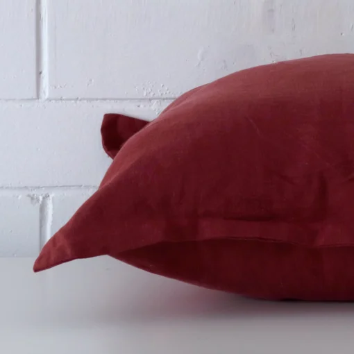 Horizontal edge of large cushion cover is shown. The linen fabric and rust tone can be seen from this side view.