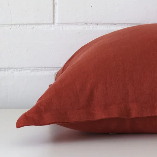 A large terracotta cushion cover is laid flat. This angle shows the side of the linen fabric up close.