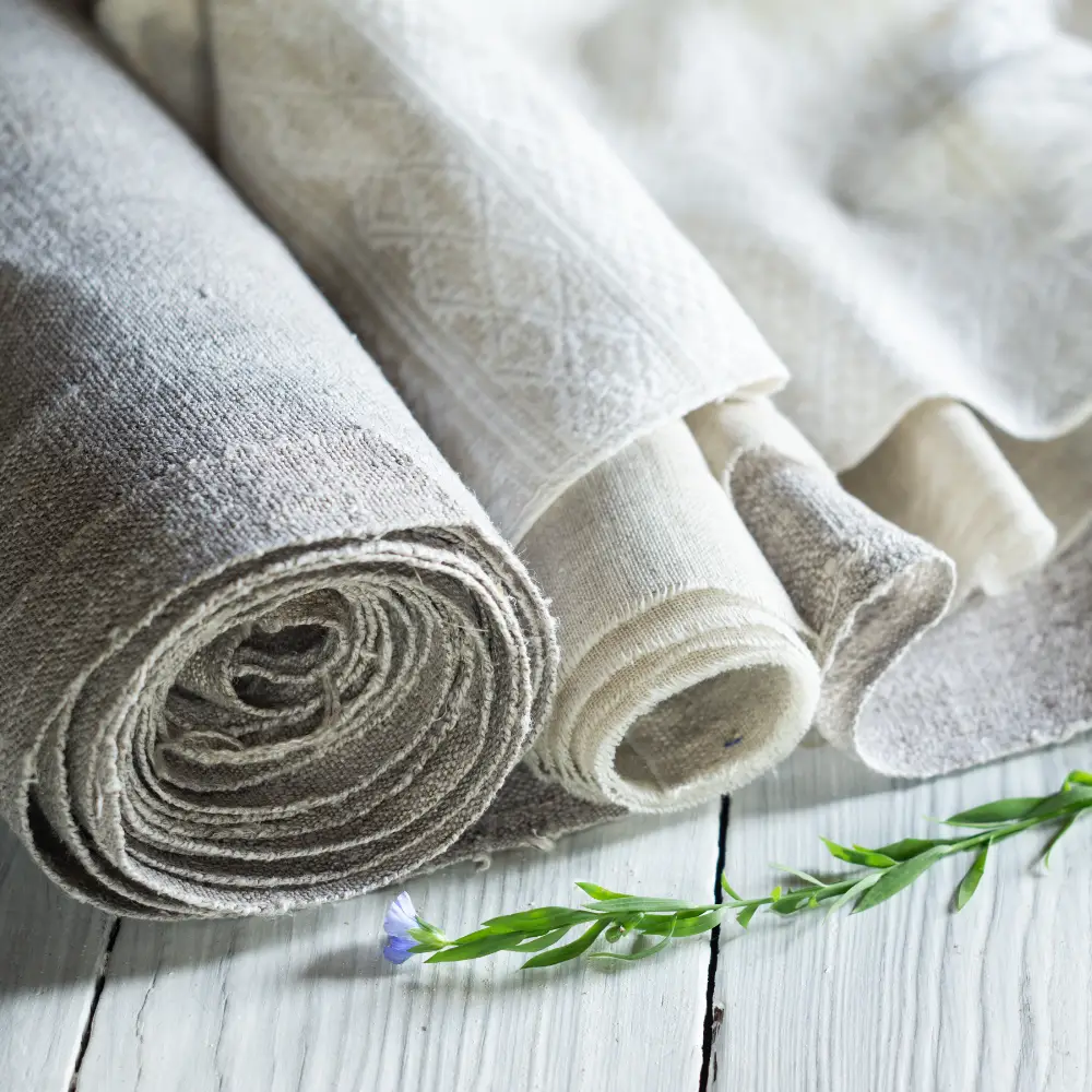 A small purple flower of a flax plant is next to folds of lovely linen fabric.
