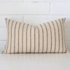 A brick wall that has a striped cushion cover positioned in front of it. It has an exquisite designer material and a lovely rectangle shape.