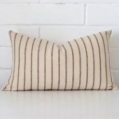 A brick wall that has a striped cushion cover positioned in front of it. It has an exquisite designer material and a lovely rectangle shape.
