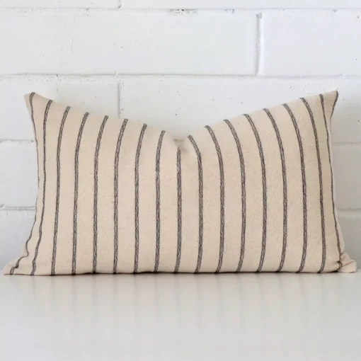 A brick wall that has a striped cushion cover positioned in front of it. It has an exquisite designer material and a lovely rectangle shape.