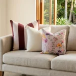 Trio of cushions with a mulberry stripe, soft cream, and a bold floral print, on a couch.