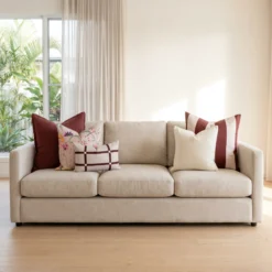 Five cushions featuring burgundy linen, a mulberry stripe, soft cream, a bold floral print, and a checked lumbar, on a sofa.