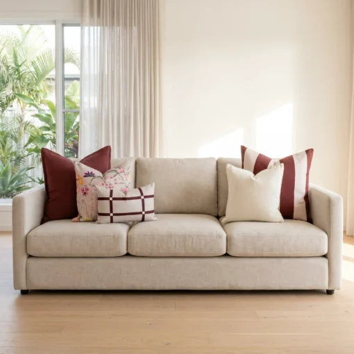 Five cushions featuring burgundy linen, a mulberry stripe, soft cream, a bold floral print, and a checked lumbar, on a sofa.