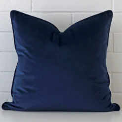 A lovely large blue cushion cover arranged in front of a white wall. It is made from a soft velvet material.
