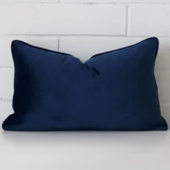 A brick wall that has a royal blue cushion cover positioned in front of it. It has an exquisite velvet material and a lovely rectangle shape.