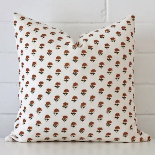Terracotta floral cushion positioned in front of a brick wall. It has a square shape and is made from a linen material.