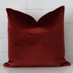 A hero shot of a square cushion cover. It is made from a deluxe velvet fabric and features a rust colour.