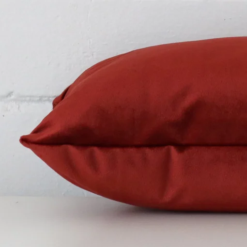 A rust cushion positioned on its back panel. The shot shows a lateral view of the velvet fabric and its square size.