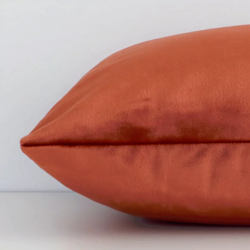 A rust velvet cushion positioned on its back panel. The shot shows a lateral view of the velvet fabric and its rectangular size.